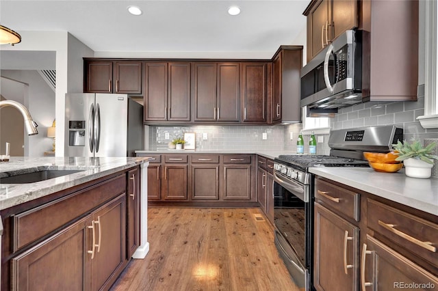 kitchen featuring a sink, appliances with stainless steel finishes, backsplash, light stone countertops, and light wood finished floors