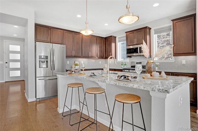 kitchen featuring an island with sink, light wood-style flooring, appliances with stainless steel finishes, a kitchen breakfast bar, and pendant lighting