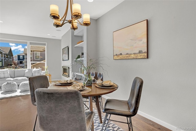 dining room with an inviting chandelier, a warm lit fireplace, baseboards, and wood finished floors