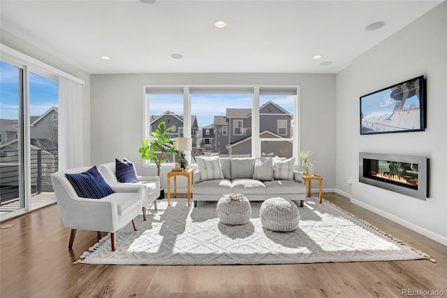 living area featuring a glass covered fireplace, recessed lighting, wood finished floors, and baseboards