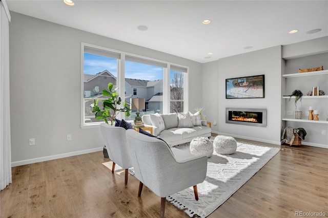 living area featuring light wood-type flooring, a glass covered fireplace, and baseboards