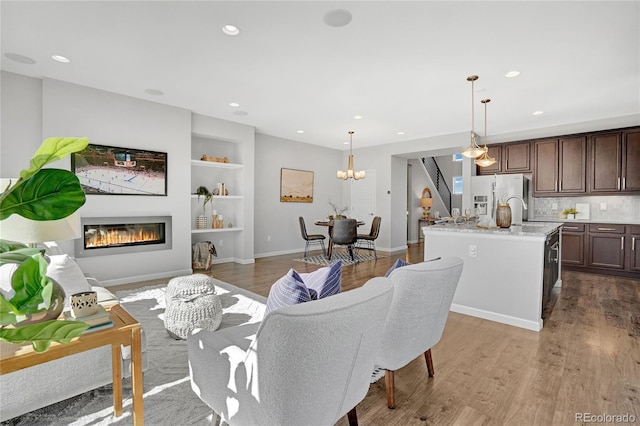 living area featuring a notable chandelier, recessed lighting, wood finished floors, built in features, and a glass covered fireplace