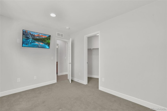 unfurnished bedroom featuring carpet floors, a walk in closet, visible vents, and baseboards