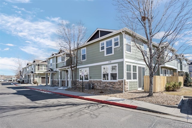 townhome / multi-family property with stone siding, a residential view, fence, and cooling unit