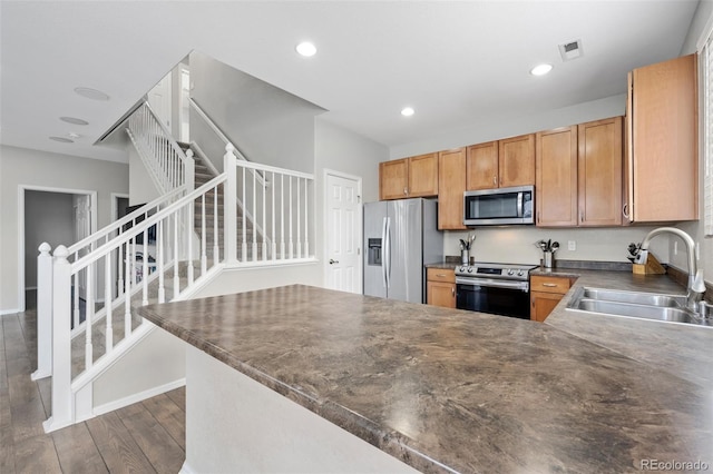 kitchen featuring recessed lighting, dark wood-type flooring, a sink, appliances with stainless steel finishes, and dark countertops