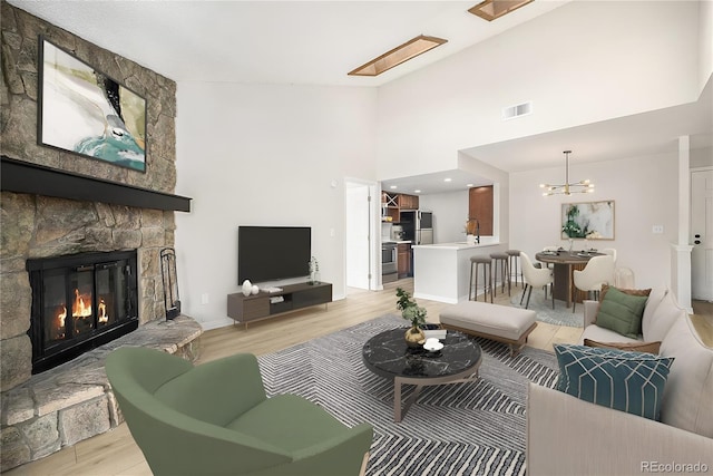 living room with high vaulted ceiling, a stone fireplace, sink, light hardwood / wood-style flooring, and a notable chandelier