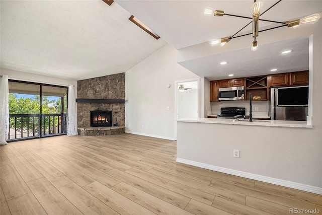 unfurnished living room featuring a fireplace, ceiling fan with notable chandelier, light hardwood / wood-style flooring, and lofted ceiling