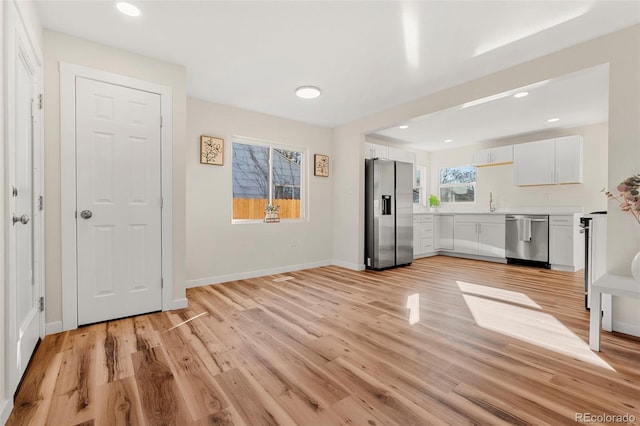 kitchen with light wood-style flooring, baseboards, white cabinets, light countertops, and appliances with stainless steel finishes