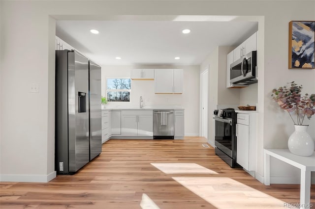 kitchen featuring baseboards, white cabinets, appliances with stainless steel finishes, light wood-type flooring, and recessed lighting