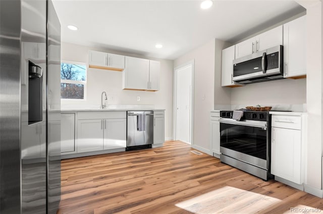 kitchen with light wood-style flooring, recessed lighting, stainless steel appliances, white cabinetry, and light countertops