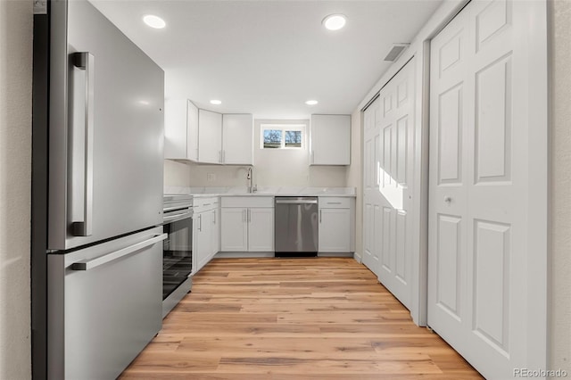 kitchen featuring white cabinets, light wood-style flooring, stainless steel appliances, light countertops, and recessed lighting