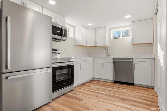 kitchen with recessed lighting, white cabinets, appliances with stainless steel finishes, light wood-type flooring, and light stone countertops