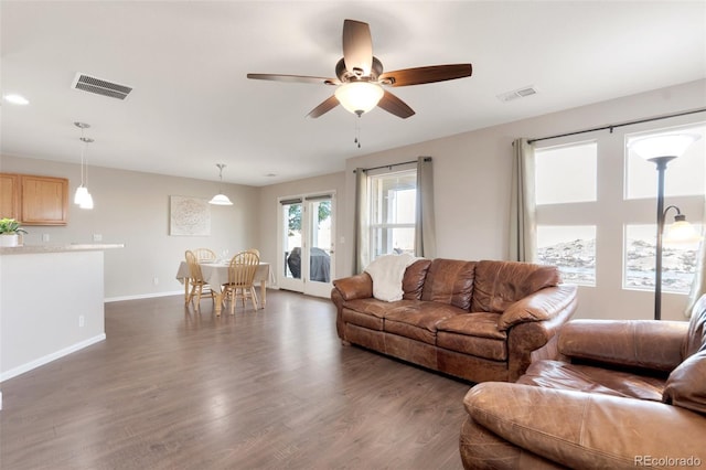 living area with dark wood-type flooring, visible vents, baseboards, and a ceiling fan