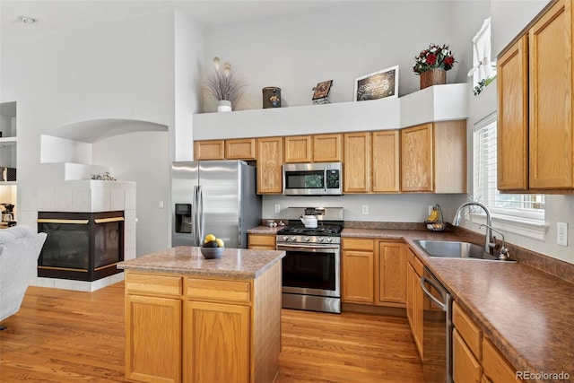 829 Sanctuary Cir, Longmont, CO 80504 - kitchen featuring appliances with stainless steel finishes, a tiled fireplace, light wood finished floors, a kitchen island, and dark countertops