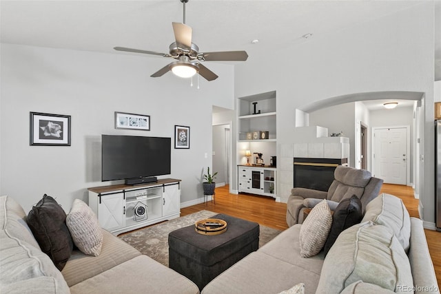 829 Sanctuary Cir, Longmont, CO 80504 - living area featuring arched walkways, built in features, light wood-type flooring, ceiling fan, and a tiled fireplace