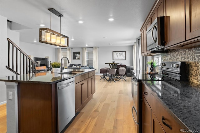 kitchen featuring a sink, stainless steel appliances, open floor plan, light wood-style floors, and backsplash