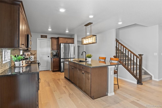 kitchen featuring stainless steel appliances, a sink, light wood-style floors, dark stone counters, and recessed lighting