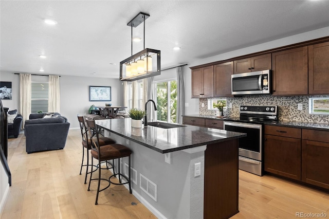 kitchen with appliances with stainless steel finishes, a sink, light wood-style flooring, a kitchen bar, and backsplash