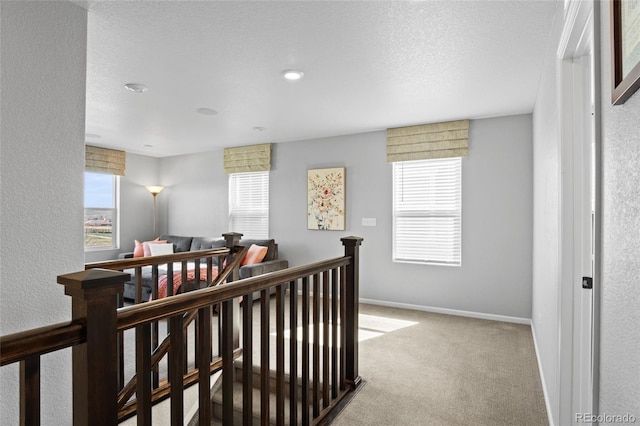 hall featuring an upstairs landing, carpet, baseboards, and a textured ceiling