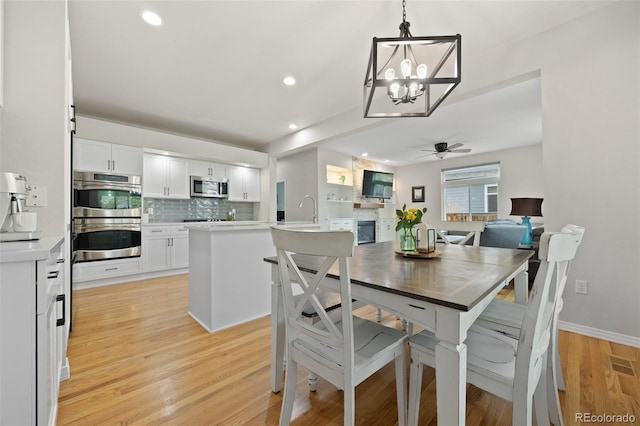 dining room with a stone fireplace, baseboards, recessed lighting, light wood-type flooring, and ceiling fan with notable chandelier