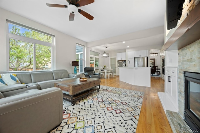 living room featuring light wood-style floors, a ceiling fan, and a glass covered fireplace