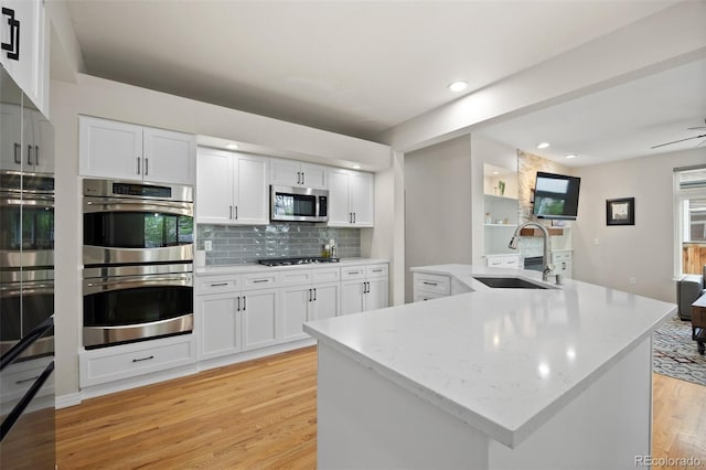 kitchen featuring white cabinets, appliances with stainless steel finishes, a sink, light wood finished floors, and tasteful backsplash