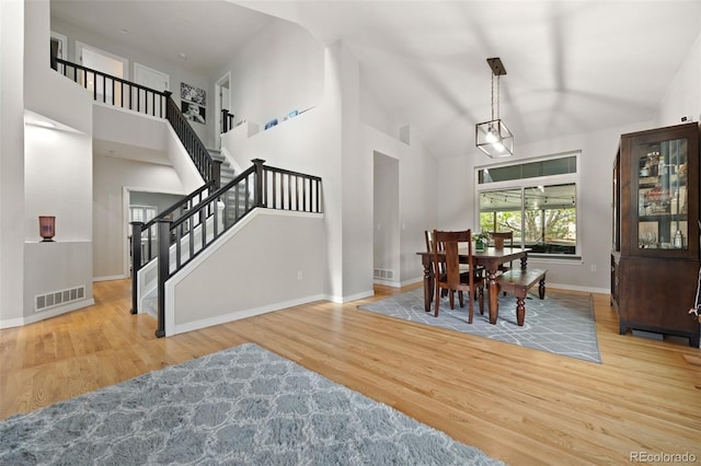 dining area with stairway, high vaulted ceiling, wood finished floors, and visible vents