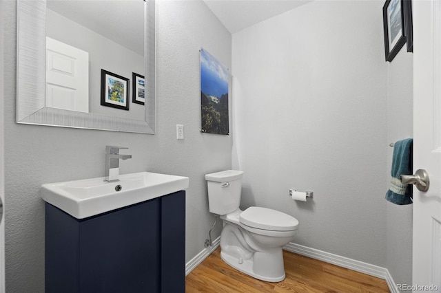 half bathroom with baseboards, vanity, toilet, and wood finished floors