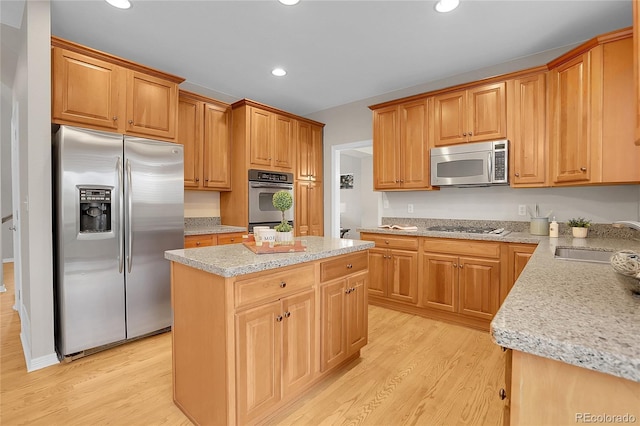 kitchen with a sink, light wood finished floors, appliances with stainless steel finishes, and a kitchen island
