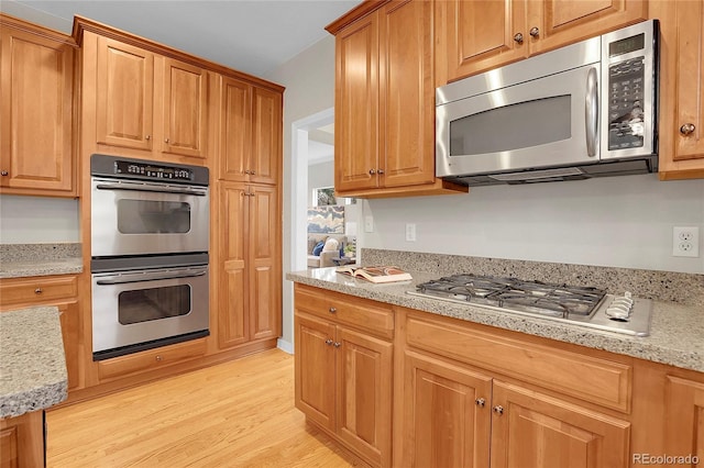 kitchen featuring light stone counters, brown cabinetry, light wood-style flooring, and stainless steel appliances