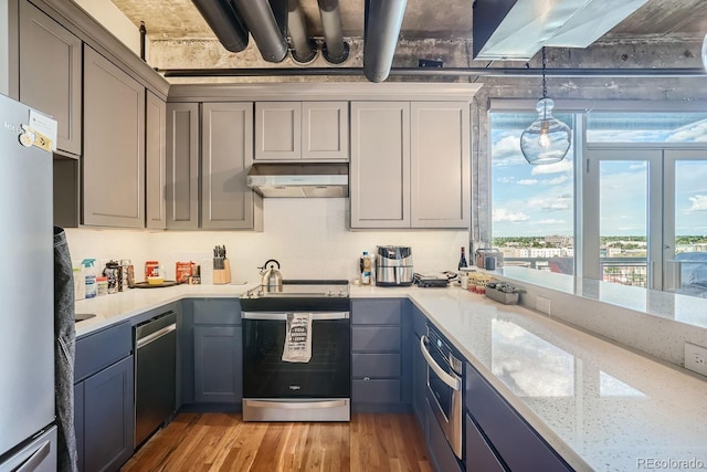 kitchen with decorative light fixtures, stainless steel appliances, light stone counters, and light hardwood / wood-style floors