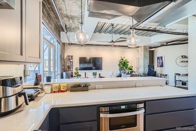 kitchen featuring light stone counters, hanging light fixtures, gray cabinetry, and stainless steel oven