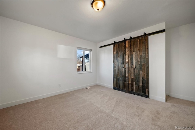 unfurnished bedroom featuring a barn door and light colored carpet