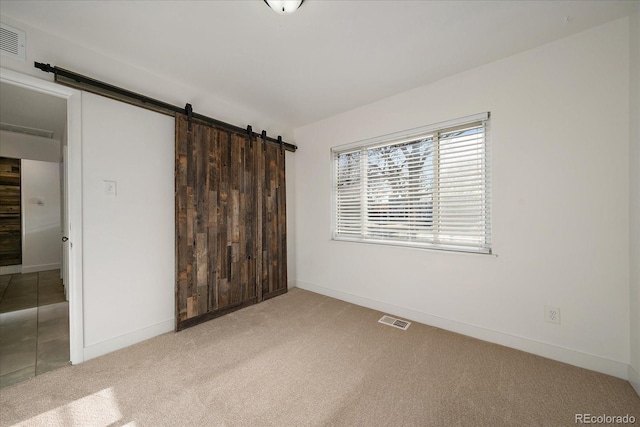 unfurnished bedroom featuring a barn door, carpet floors, and a closet