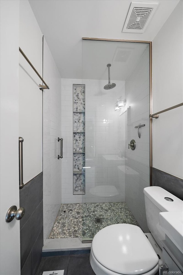 bathroom with tile patterned flooring, toilet, an enclosed shower, and tile walls