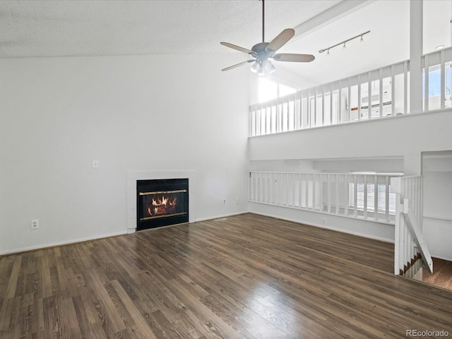 unfurnished living room with a fireplace, a high ceiling, ceiling fan, dark wood-type flooring, and a textured ceiling