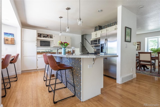 5983 W Indore Pl, Littleton, CO 80128 - kitchen with appliances with stainless steel finishes, white cabinets, light wood-style flooring, and a kitchen breakfast bar