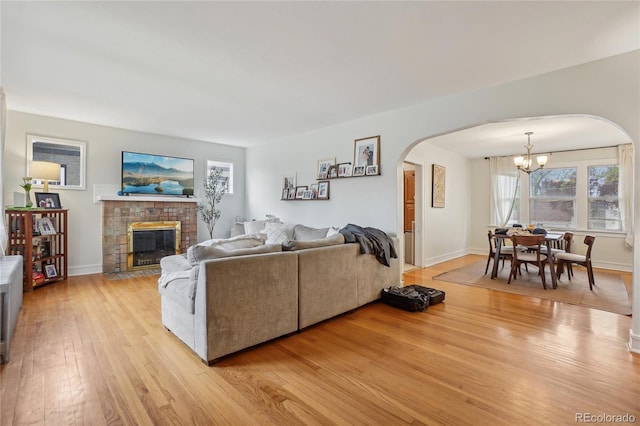 living room with arched walkways, a chandelier, light wood finished floors, a fireplace with flush hearth, and baseboards