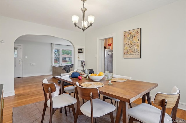 dining space featuring arched walkways, light wood-style flooring, a chandelier, and baseboards