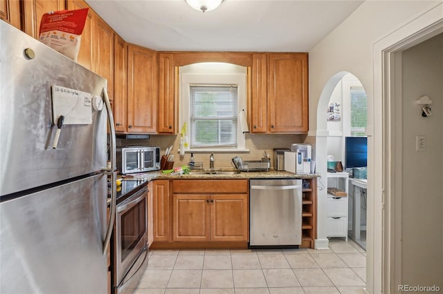 kitchen with appliances with stainless steel finishes, light stone counters, decorative backsplash, light tile patterned floors, and arched walkways