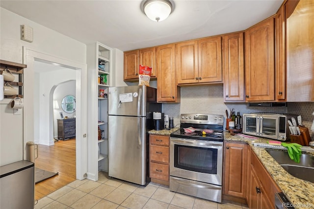 kitchen featuring stainless steel appliances, light tile patterned floors, decorative backsplash, and light stone counters
