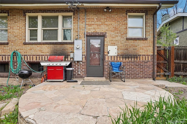doorway to property featuring brick siding, a patio, and fence