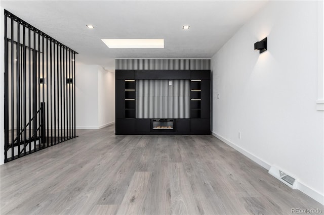 spare room with a glass covered fireplace, visible vents, light wood-style flooring, and baseboards