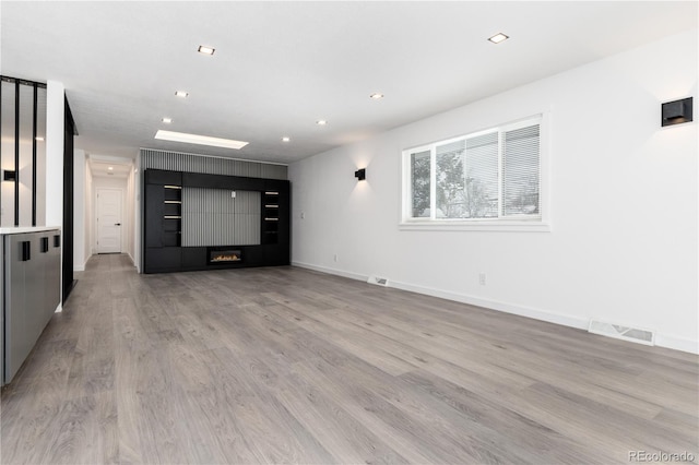 unfurnished living room with recessed lighting, visible vents, light wood-style flooring, a glass covered fireplace, and baseboards