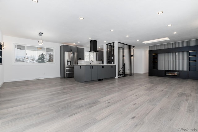 unfurnished living room featuring light wood-style flooring, recessed lighting, a sink, baseboards, and a glass covered fireplace