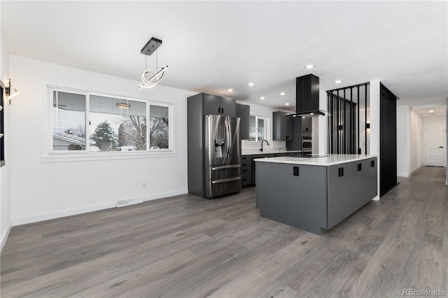 kitchen featuring a center island, pendant lighting, island exhaust hood, light countertops, and appliances with stainless steel finishes