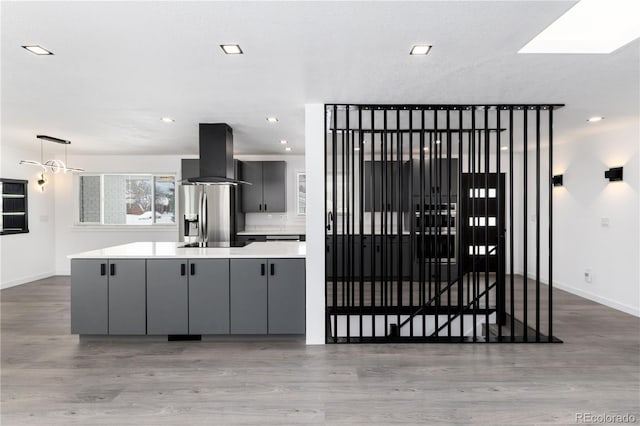 kitchen with island exhaust hood, gray cabinetry, light countertops, modern cabinets, and stainless steel fridge