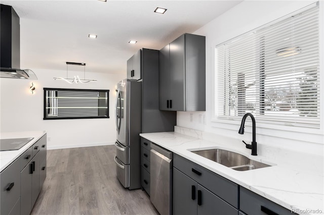 kitchen with decorative light fixtures, gray cabinets, appliances with stainless steel finishes, a sink, and wall chimney exhaust hood