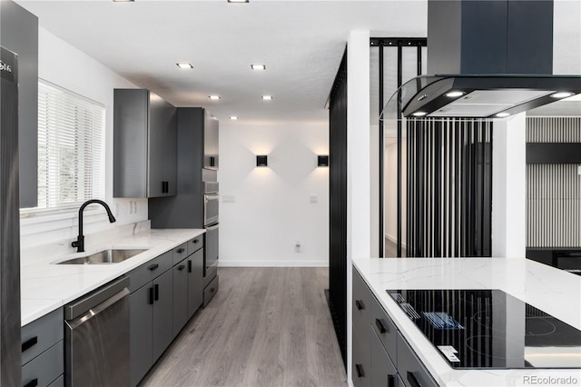 kitchen with light wood finished floors, appliances with stainless steel finishes, light stone countertops, gray cabinets, and a sink