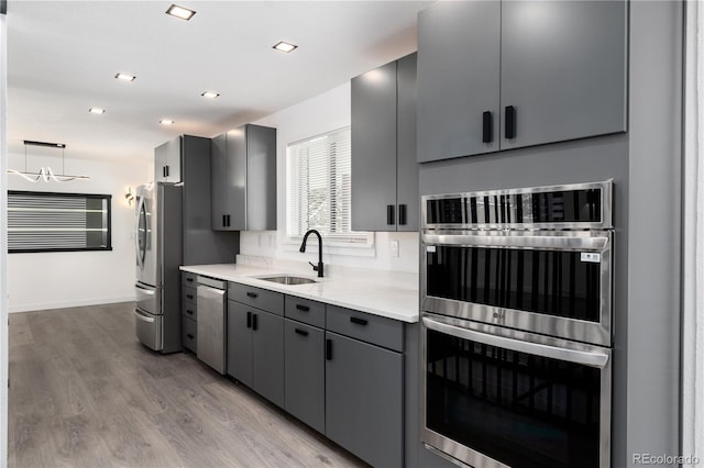 kitchen featuring stainless steel appliances, hanging light fixtures, light wood-style flooring, gray cabinetry, and a sink